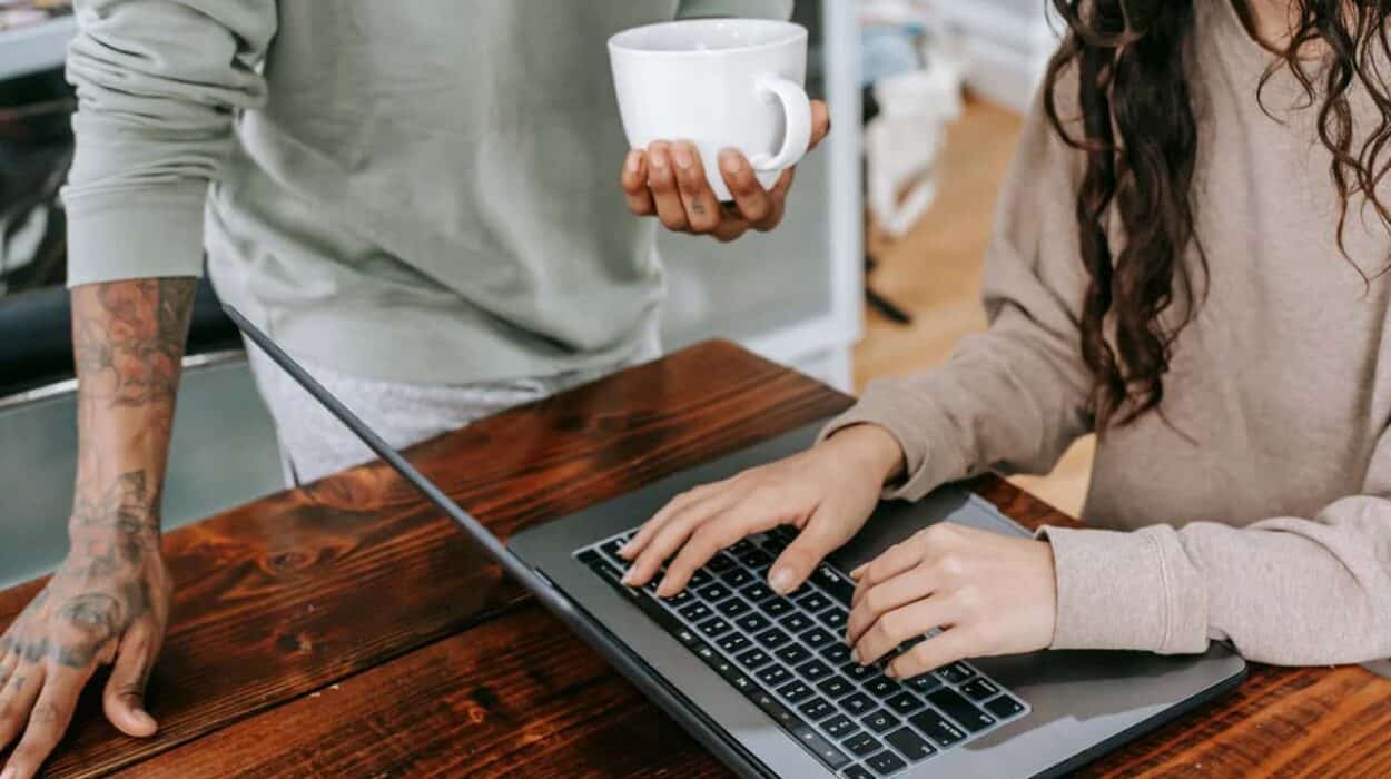 Two people working. One on a laptop and one holding a white mug of coffee
