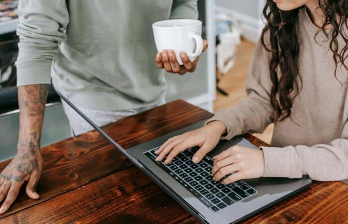 Two people working. One on a laptop and one holding a white mug of coffee